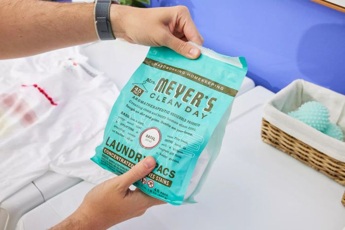 A person is shown holding a pack of Mrs. Meyer’s Clean Day Laundry Detergent Pacs.