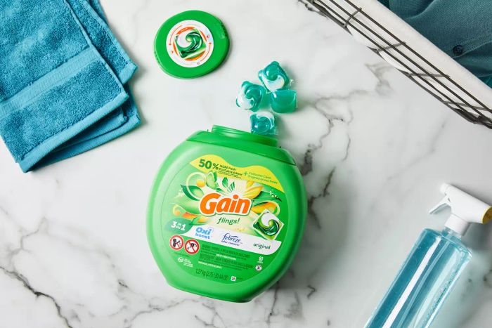 Gain Original Flings Laundry Detergent Pods arranged on a marble countertop, surrounded by a towel and spray bottle