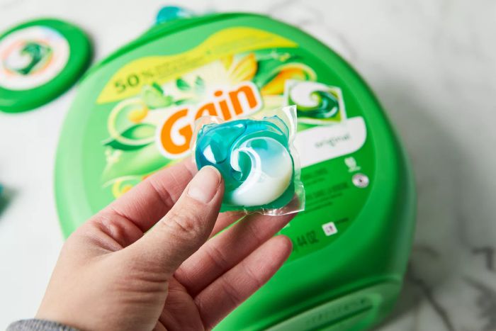 A hand is seen holding a Gain Original Flings Laundry Detergent pod above a container