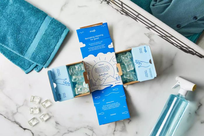 Dropps Sensitive Skin & Baby Laundry Detergent Pods placed on a marble counter, accompanied by a towel and a spray bottle.