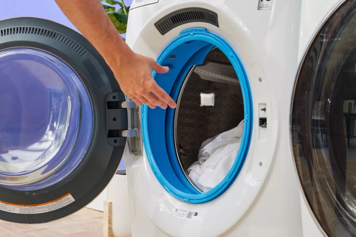 A person is placing a piece of clothing into the washing machine to clean it using Mrs. Meyer’s Clean Day Laundry Detergent Pacs.