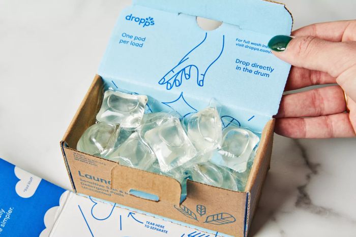 A person is holding a box of Dropps Sensitive Skin & Baby Laundry Detergent Pods on a marble counter.