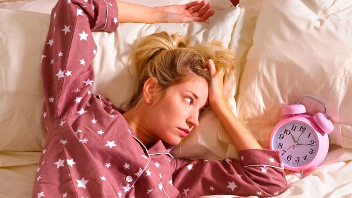 A woman lying on her bed, her eyes fixed on the ticking clock.