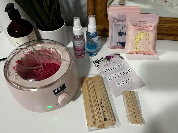 A reviewer’s waxing kit with heater, beads, strips, application sticks, and an instruction manual neatly arranged on a counter