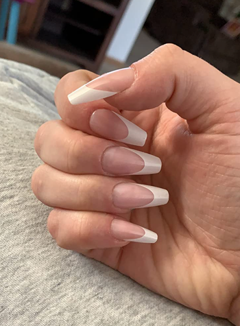 Reviewer showing off press-on clear nails with white tips