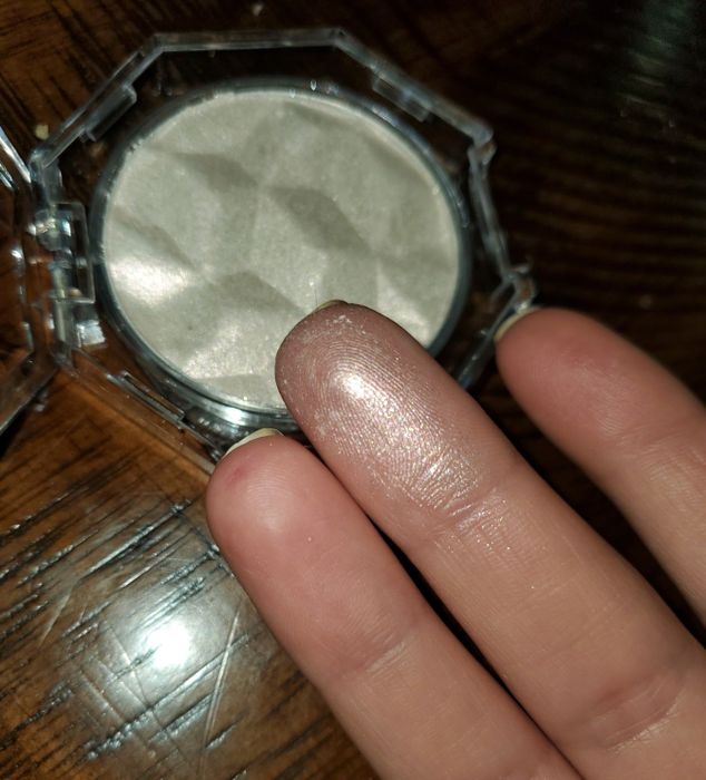 The compact with a finger dipped in the product, showing off its glow