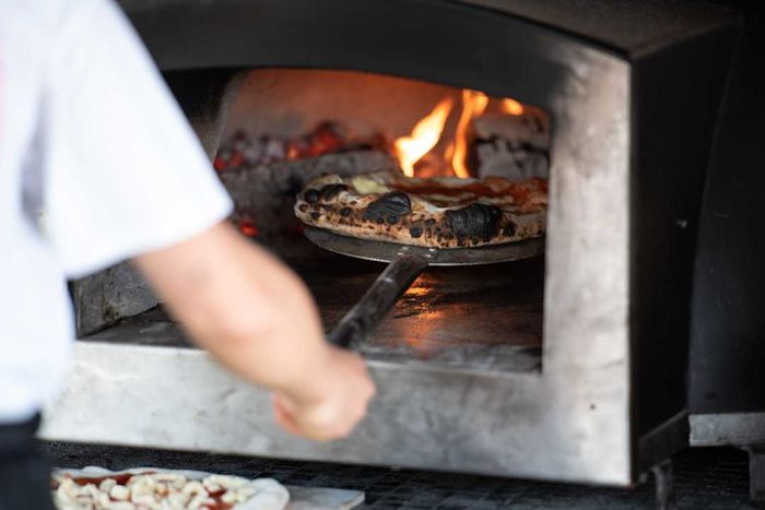 A person placing pizza into a wood-fired oven.