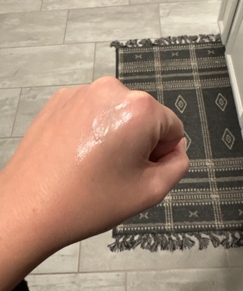 A person applying a clear gel to the back of their hand from the jar of cleansing balm