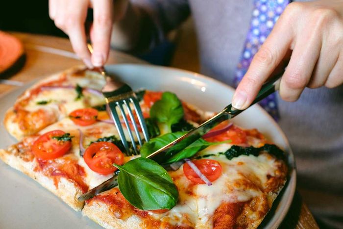 A close-up image of someone using a knife and fork to slice and eat pizza