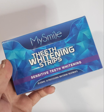 A hand holding a box of MySmile Teeth Whitening Strips, designed for sensitive teeth