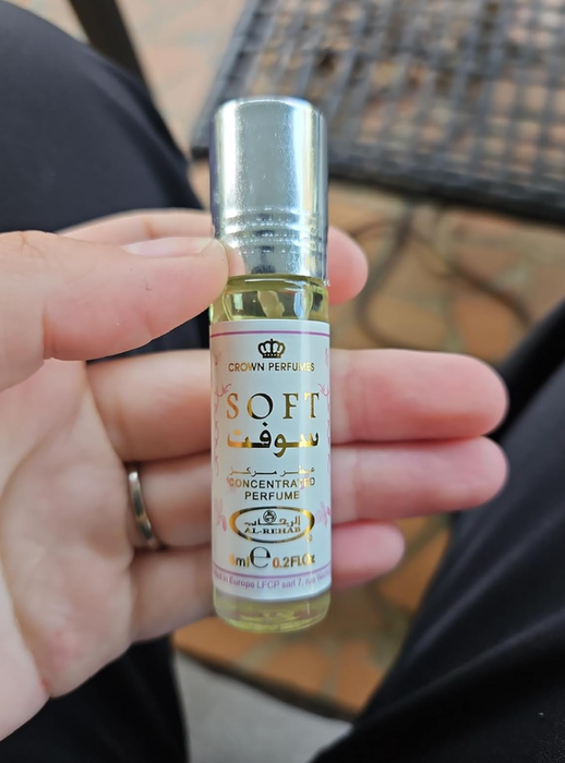 A hand gripping a small bottle of Crown Perfumes' signature fragrance.