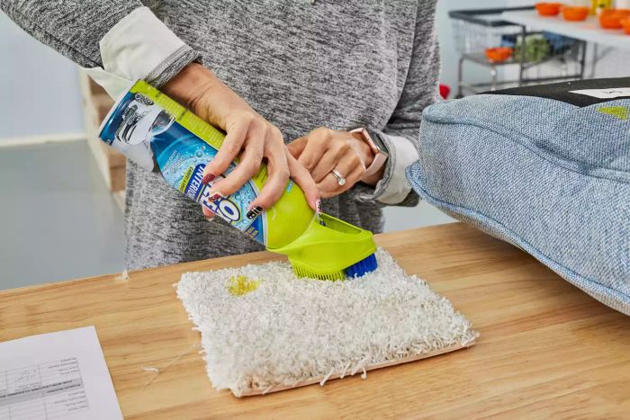 A person scrubs a carpet using the brush attached to the OxiClean Total Interior Carpet & Upholstery Cleaner bottle