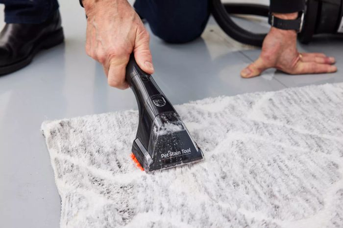 An individual utilizing the handheld attachment of a Bissell ProHeat 2X Revolution Pet Carpet Cleaner 35799 on a carpet