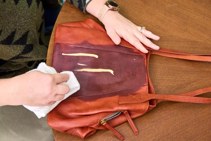 A person applies the Chemical Guys Leather Cleaner and Conditioner Complete Leather Care Kit to a leather bag