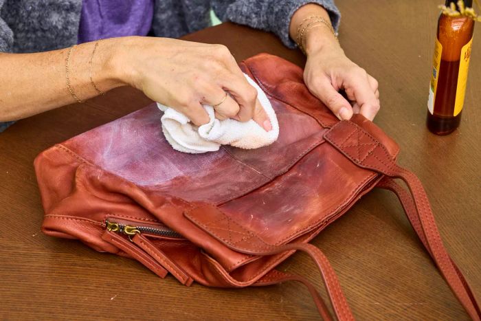 An individual cleans a leather bag with Leather Honey Leather Cleaner