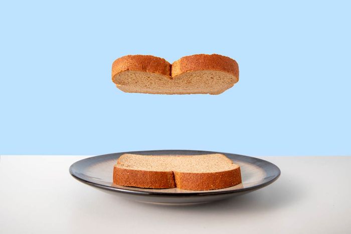 A single slice of bread hovering above another on a ceramic plate against a white table and blue background