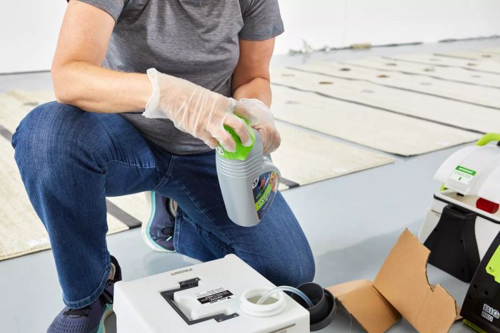 A person securing the lid on a bottle of cleaning solution near the tank of the Bissell Big Green Pet Pro Carpet Cleaner.