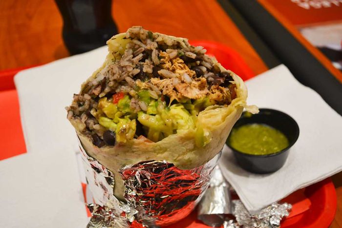 A burrito filled with meat, rice, beans, and vegetables, wrapped in aluminum foil