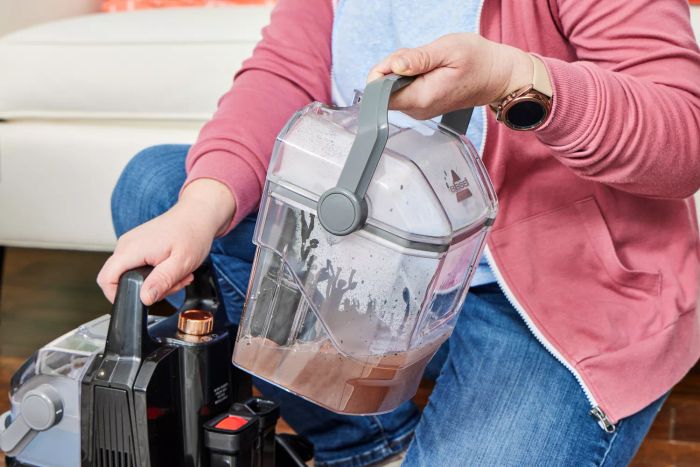 A person detaching the dirty water tank from the Bissell Little Green HydroSteam Pet Carpet Cleaner.