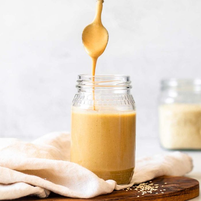 A cropped hand of a woman lifting a spoonful of tahini from a jar