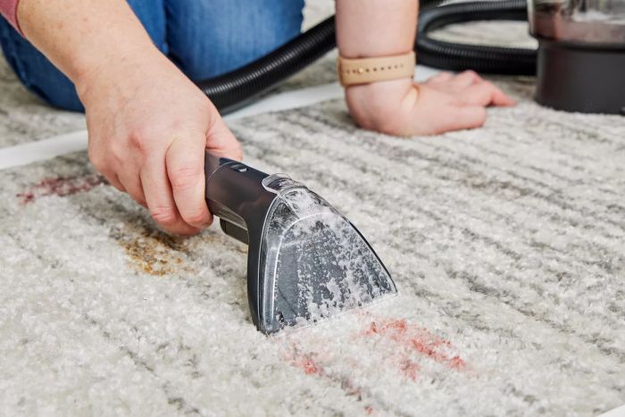 A person uses the Bissell Little Green Cordless Portable Carpet Cleaner to clean a rug