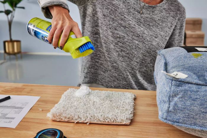 A person sprays OxiClean Total Interior Carpet & Upholstery Cleaner onto a carpet sample