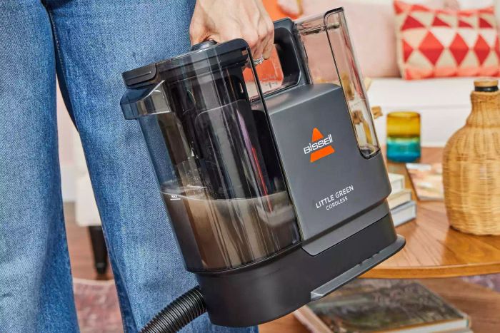 A user picks up the Bissell Little Green Cordless Portable Carpet Cleaner 3682