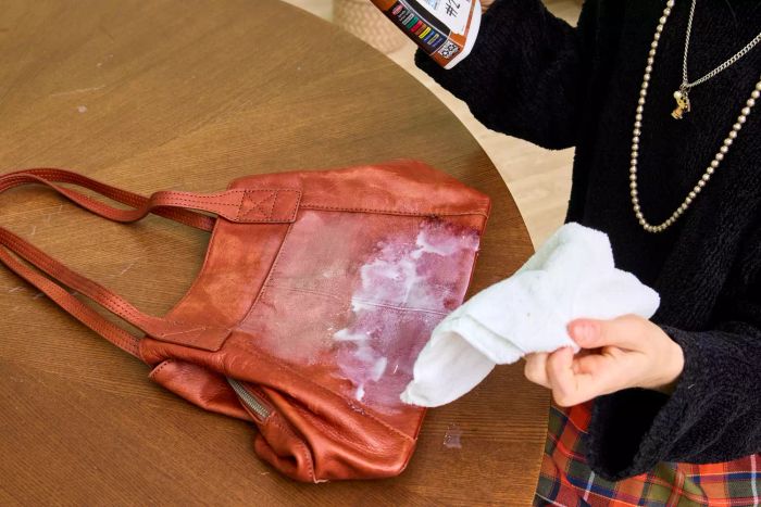 A person uses Weiman Leather Cleaner and Conditioner Spray on a leather bag