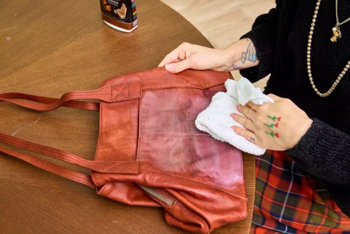 Someone applies Weiman Leather Cleaner and Conditioner Spray to a leather bag
