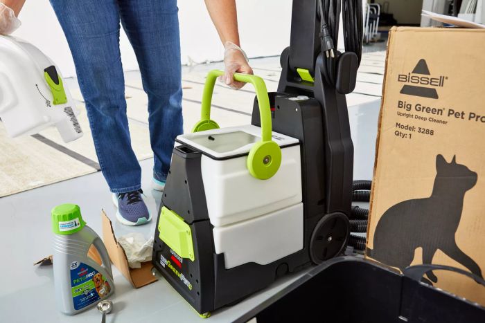 A person gripping the handle of the water tank on the Bissell Big Green Pet Pro Carpet Cleaner.