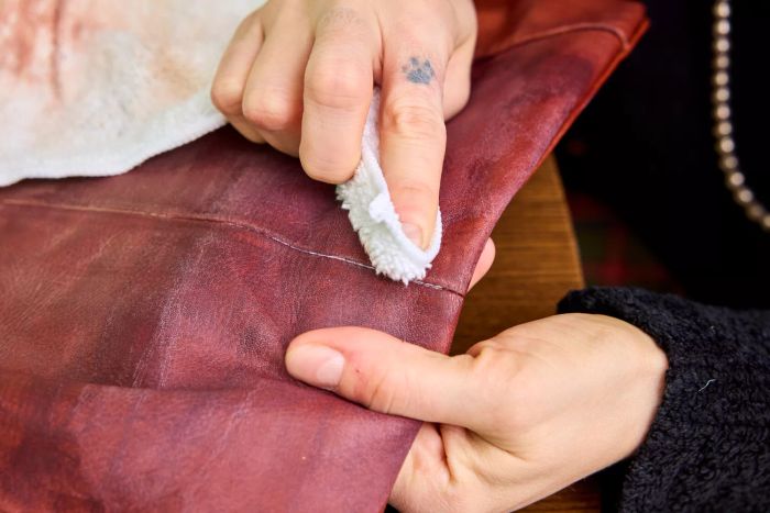 An individual works Weiman Leather Cleaner and Conditioner Spray into a leather bag