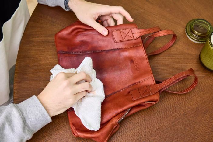 An individual uses Leather CPR 2-in-1 Leather Cleaner & Leather Conditioner on a leather handbag