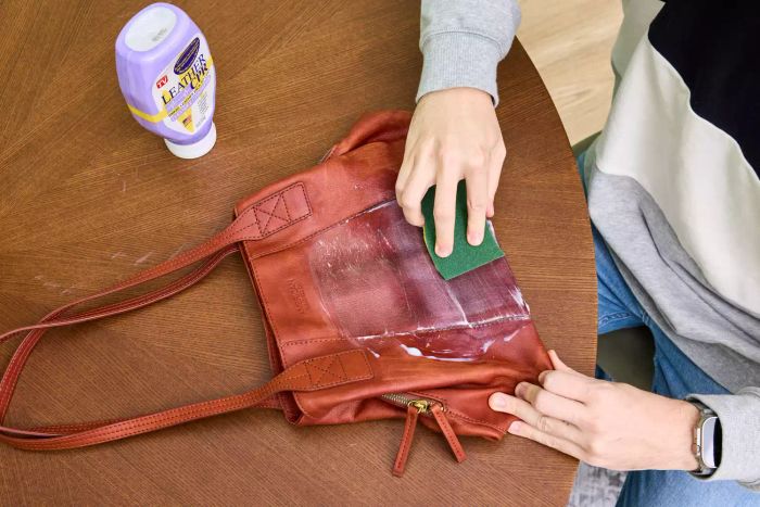 An individual works Leather CPR 2-in-1 Leather Cleaner & Leather Conditioner into a leather bag