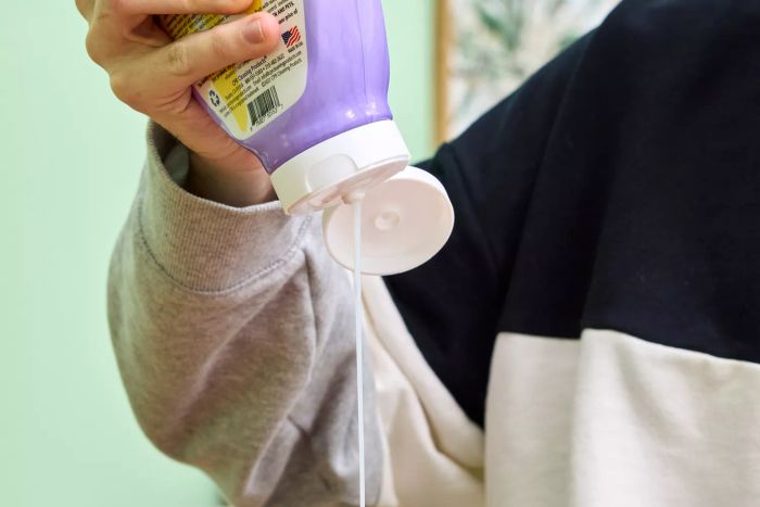 Someone squeezes the bottle of Leather CPR 2-in-1 Leather Cleaner & Leather Conditioner