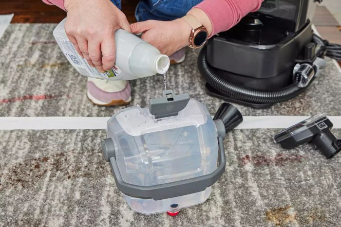 A person filling the water tank of the Bissell Little Green HydroSteam Pet Carpet Cleaner with liquid