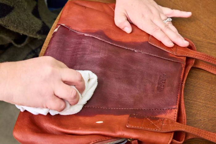 An individual uses the Chemical Guys Leather Cleaner and Conditioner Complete Leather Care Kit on a leather handbag