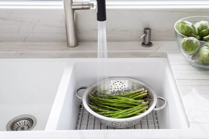 A close-up image showing fresh green asparagus and artichokes being rinsed in a modern kitchen sink, using a colander.