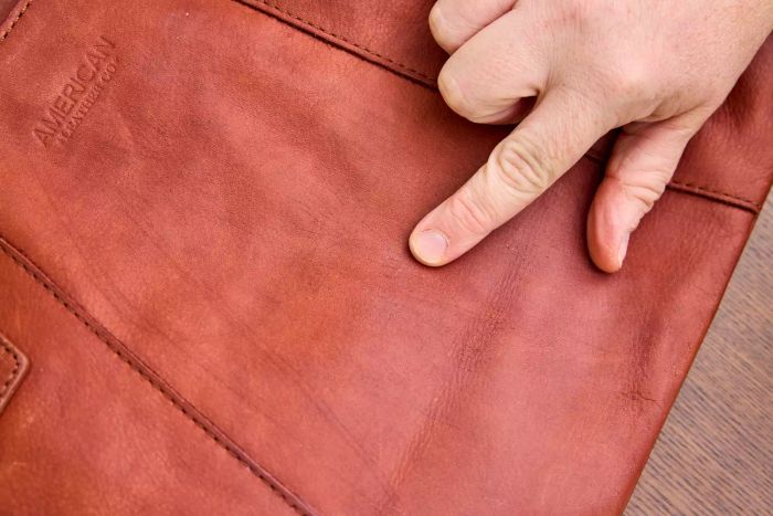 A person highlights a mark on a bag treated with Chemical Guys Leather Cleaner and Conditioner Complete Leather Care