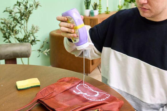 An individual applies Leather CPR 2-in-1 Leather Cleaner & Leather Conditioner to a leather handbag