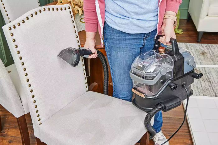 A person holding the Bissell Little Green HydroSteam Pet Carpet Cleaner above a cleaned chair.