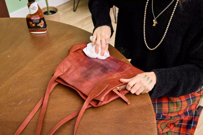 A person uses Weiman Leather Cleaner and Conditioner Spray on a leather bag