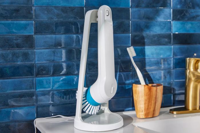 A Black+Decker Grimebuster Pro Power Scrubber Brush, placed on its stand, sits on a bathroom sink