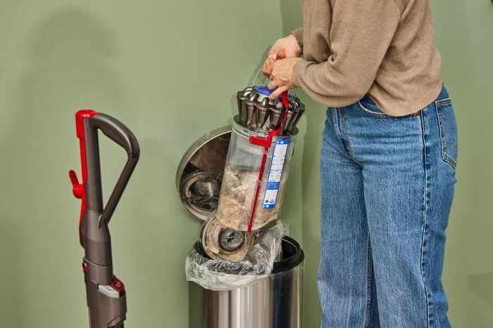 A person disposing of dirt from the Dyson Ball Animal 3 Extra into a garbage bin