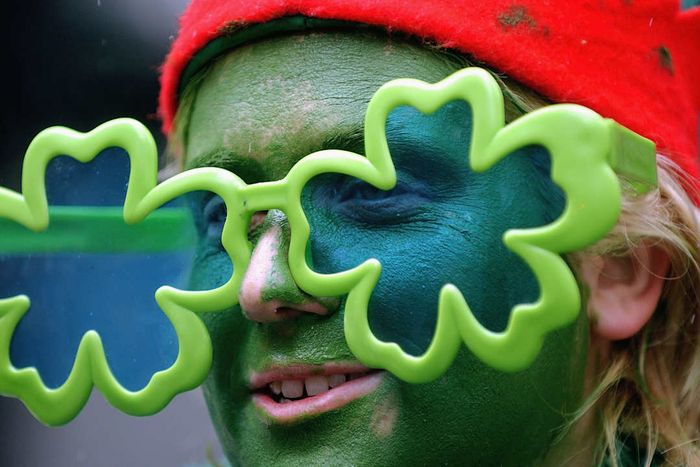 An individual wearing green face paint and shamrock-themed sunglasses