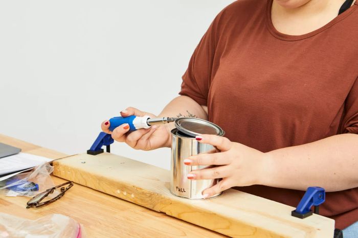 A person using the Lenox 9-in-1 Rubber Handle Multi-Bit Screwdriver to open a tin lid on a wooden table