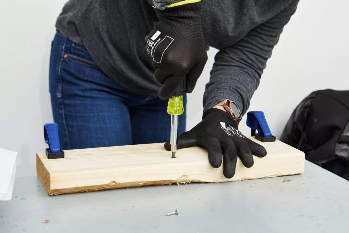 Close-up of a person using the Klein Tools 11-in-1 Screwdriver and Nut Driver to tighten a screw on a wooden piece