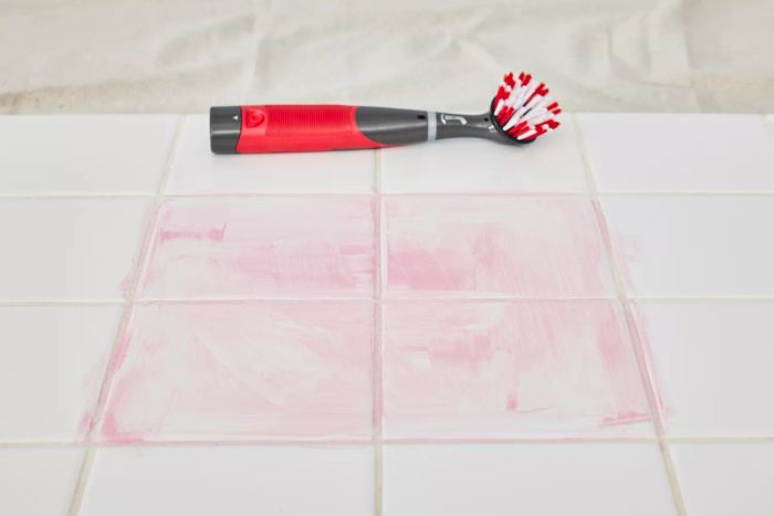 The Rubbermaid Reveal Power Scrubber is placed on white floor tile beside four sections of pink cleaning product smudges