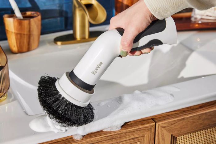 A close-up of a hand cleaning a bathroom sink using a Klever Electric Spin Scrubber with 8 Brushes