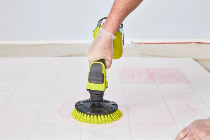 A person cleans white tile using a Ryobi One+ 18V Cordless Compact Power Scrubber