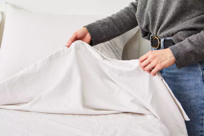 Hands arranging a bed with The Citizenry Organic Resort Cotton Sheet Set